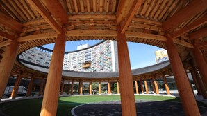 A traditional wooden pavilion with a curved roof structure, surrounded by a well-maintained lawn and a modern building with a brick facade in the background. - Lotte Buyeo Resort (Buyeo)