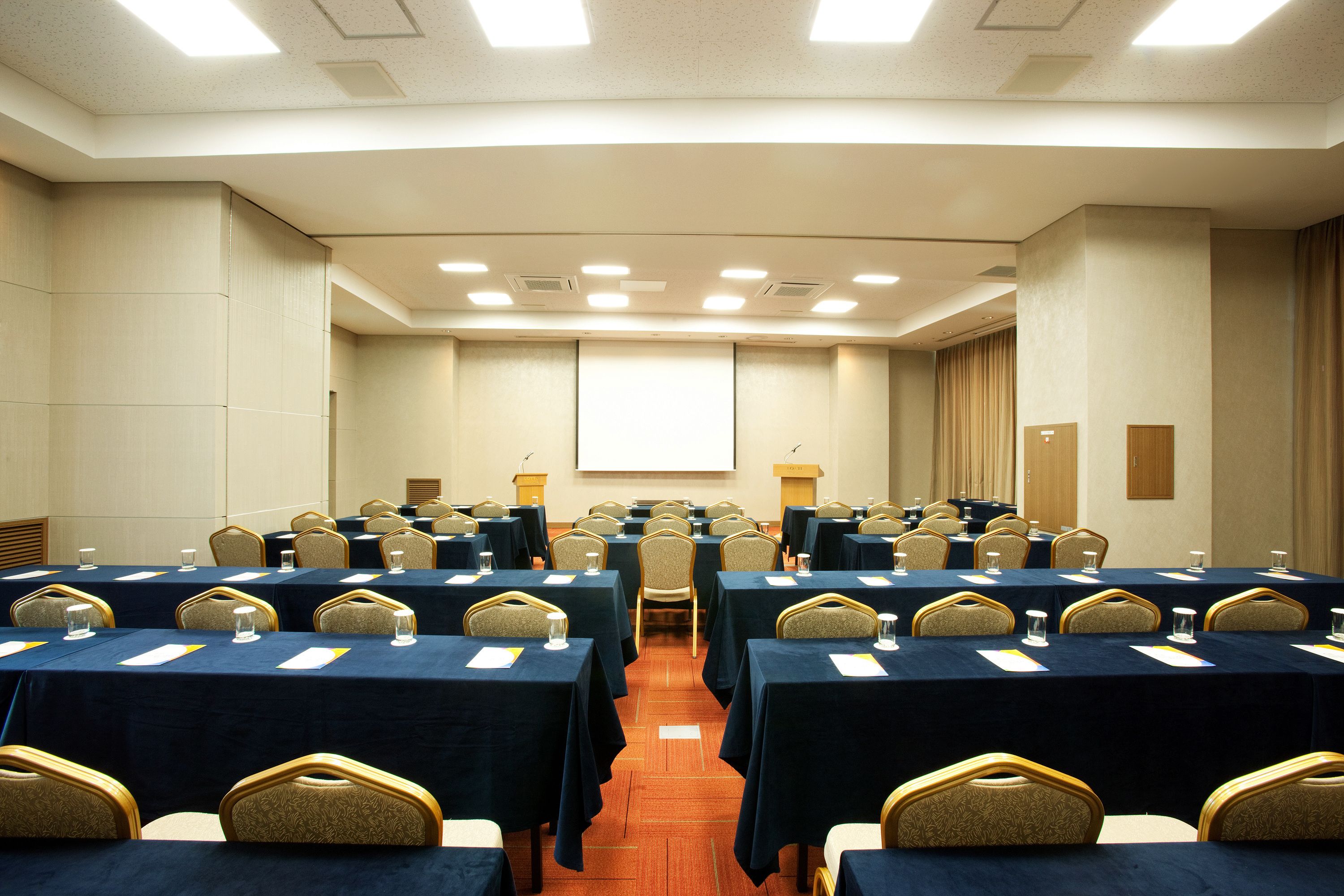 A conference room with multiple tables, chairs, and a projector screen.