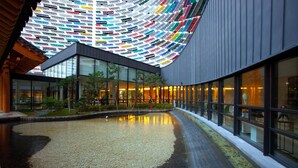 A modern building with a curved glass facade, a central courtyard with a reflective water feature, and a colorful ceiling installation. - Lotte Buyeo Resort (Buyeo)