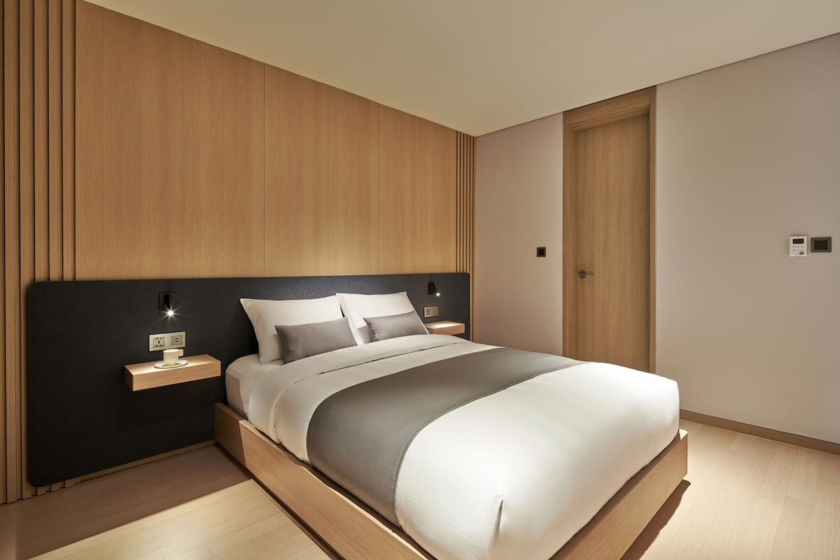 A modern bedroom with a wooden headboard, a bed with white bedding, and bedside tables with lamps.