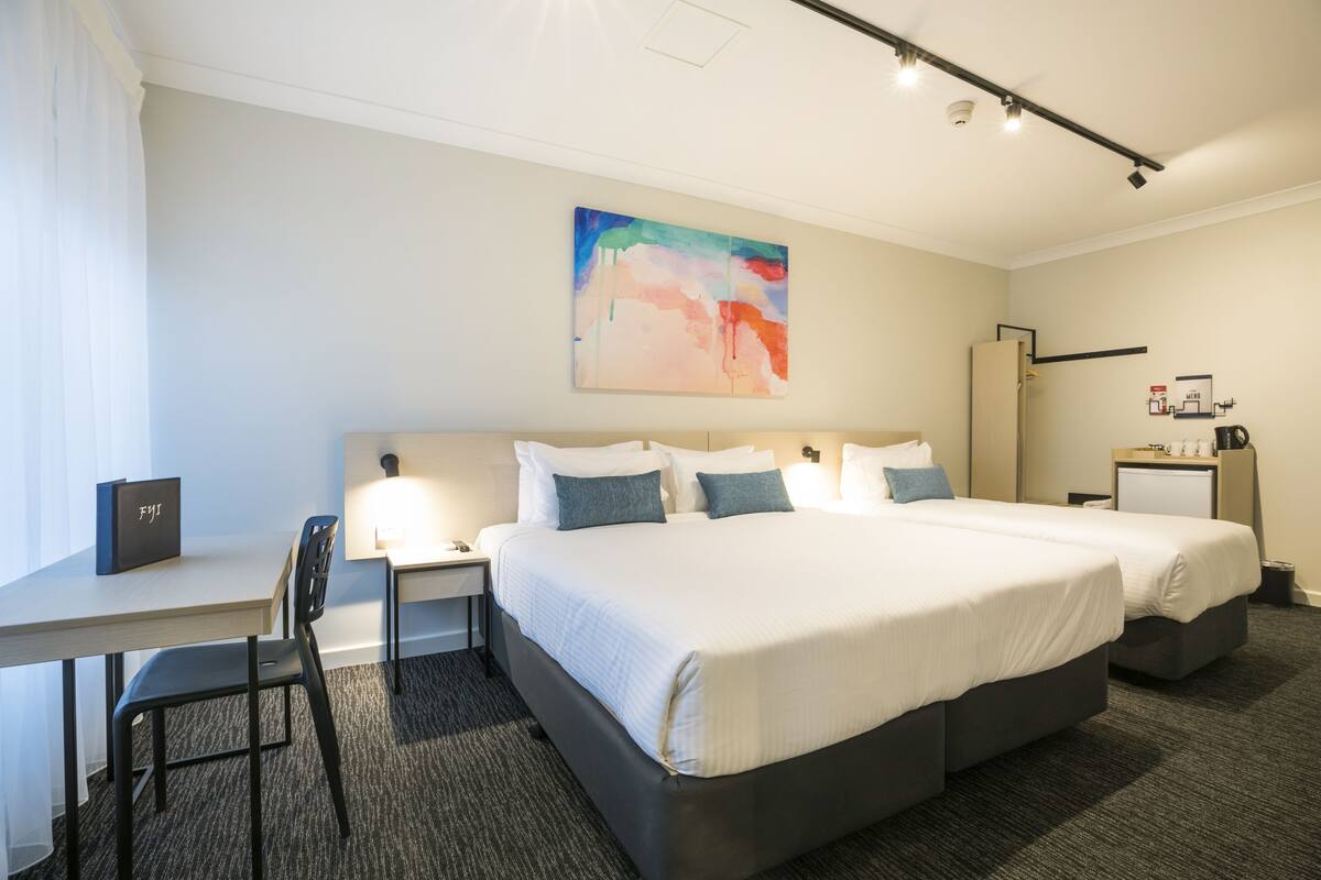 A hotel room with a large bed, a desk with a chair, a small table, and a nightstand.