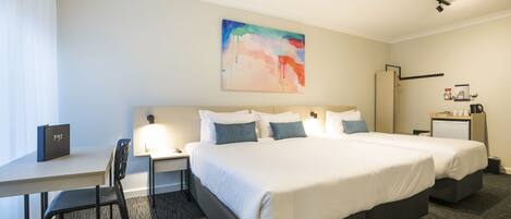A hotel room with a large bed, a desk with a chair, a small table, and a nightstand.
