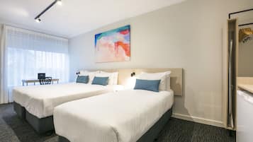 A hotel room with two beds, a desk, and a chair. There is a painting on the wall and a wardrobe with a mirror.