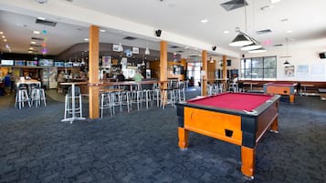 A billiards room with a pool table, bar area, and seating.