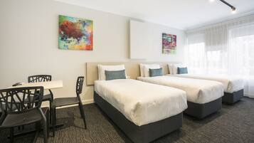 A hotel room with two beds, a desk, and chairs. There are abstract paintings on the walls.