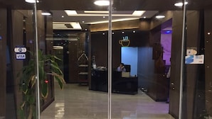 Un área de recepción moderna con puertas de vidrio, un mostrador de recepción y una planta a la vista.