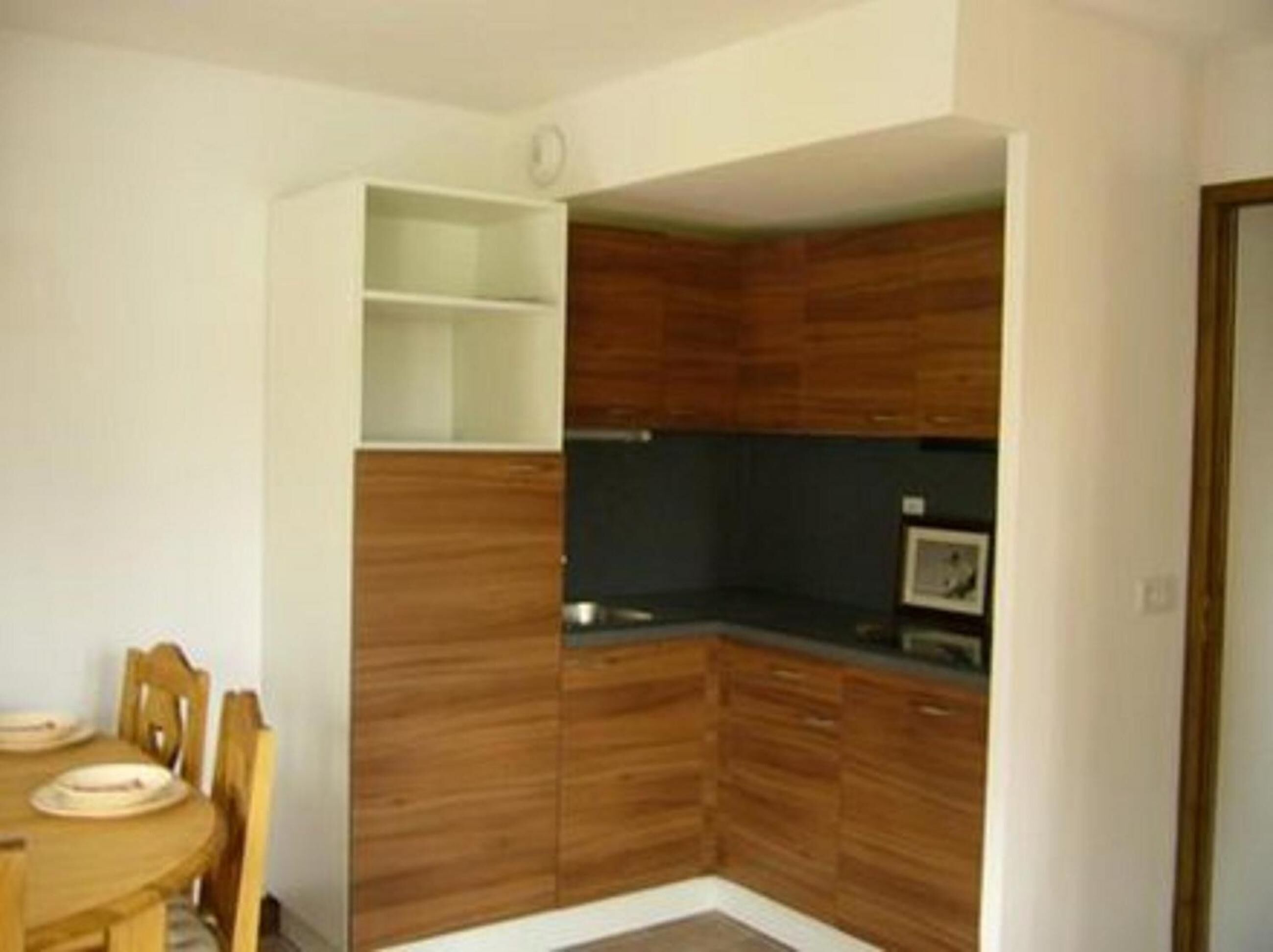 Une cuisine compacte avec des meubles en bois, un plan de travail foncé et un petit coin repas comprenant une table et des chaises.