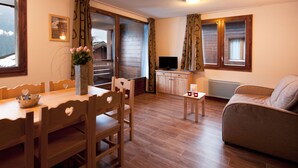 A cozy living room with a wooden dining table, chairs, a sofa, and a TV. - Résidence Lagrange Vacances Les Chalets du Mont Blanc (Hauteluce)