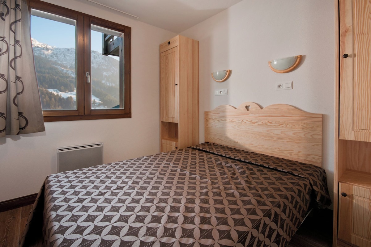 Une chambre à coucher avec un lit, une fenêtre donnant sur des montagnes enneigées, une armoire en bois et une table de chevet avec un miroir.