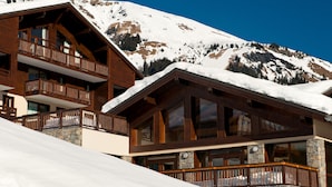 A wooden chalet with balconies and stone walls, set against a snowy mountain backdrop. - Résidence Lagrange Vacances Les Chalets du Mont Blanc (Hauteluce)