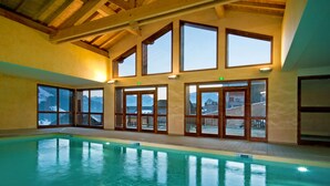 An indoor swimming pool with large windows and wooden beams. - Résidence Lagrange Vacances Les Chalets du Mont Blanc (Hauteluce)