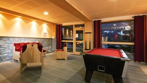 A billiards table, a pool chair, and a sofa with a red cushion in a room with a stone wall and wooden ceiling. - Résidence Lagrange Vacances Les Chalets du Mont Blanc (Hauteluce)