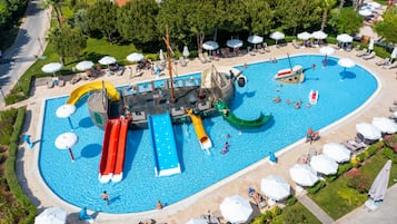 Relax by the pool surrounded by lush greenery and lounge chairs, with slides and a unique ship-shaped structure nearby.