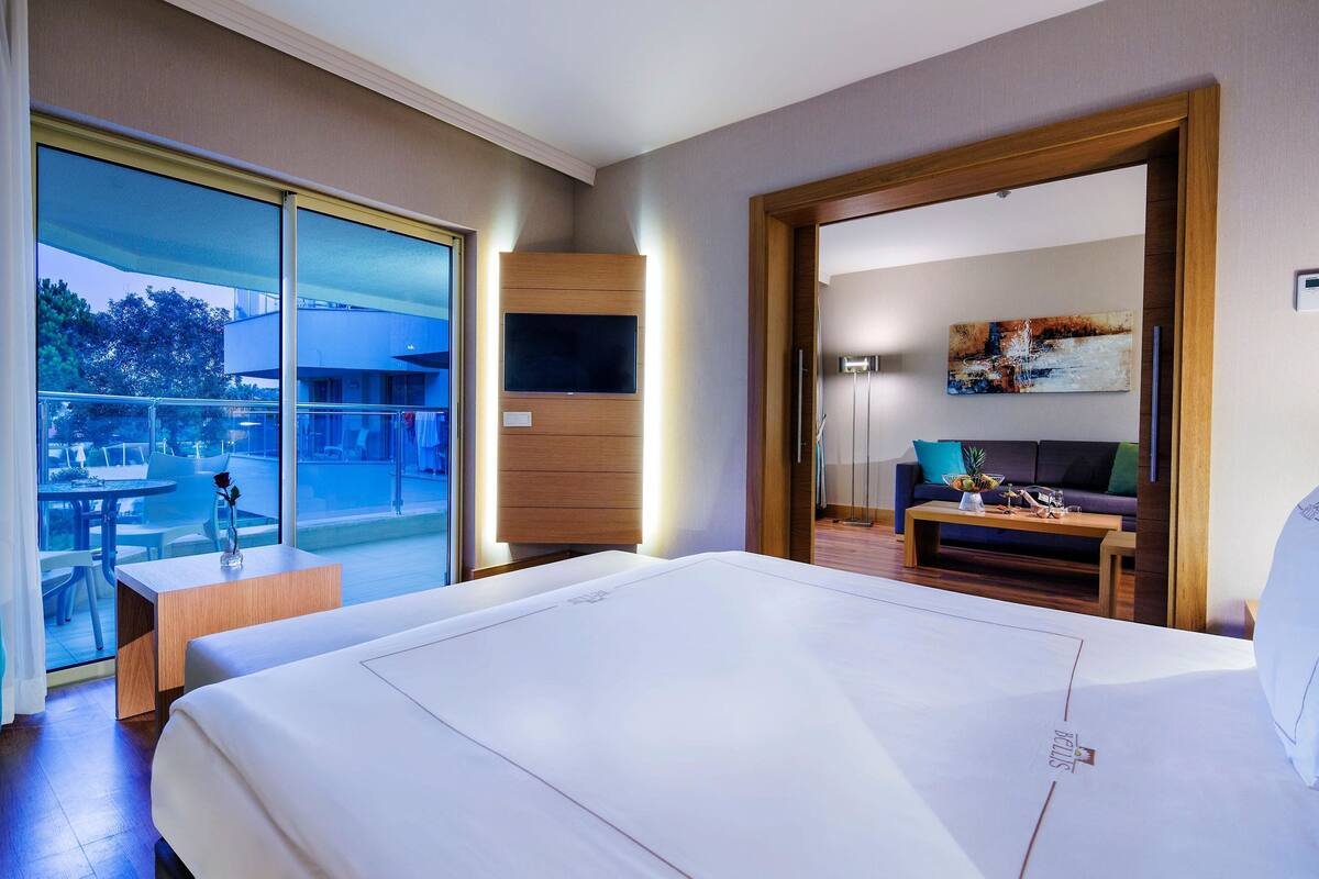 Ein Hotelzimmer mit einem großen Bett, einem Fernseher, einem Balkon mit Tisch und Stühlen sowie einem Bild an der Wand.