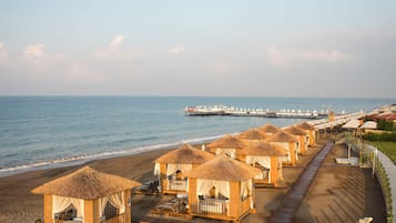 Un resort frente al mar con cabañas de techo de paja, un muelle que se adentra en el océano y un paseo marítimo a lo largo de la costa.
