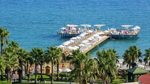 Ein Resort am Wasserufer mit einer langen Pier, Reihen von Sonnenschirmen und Palmen.