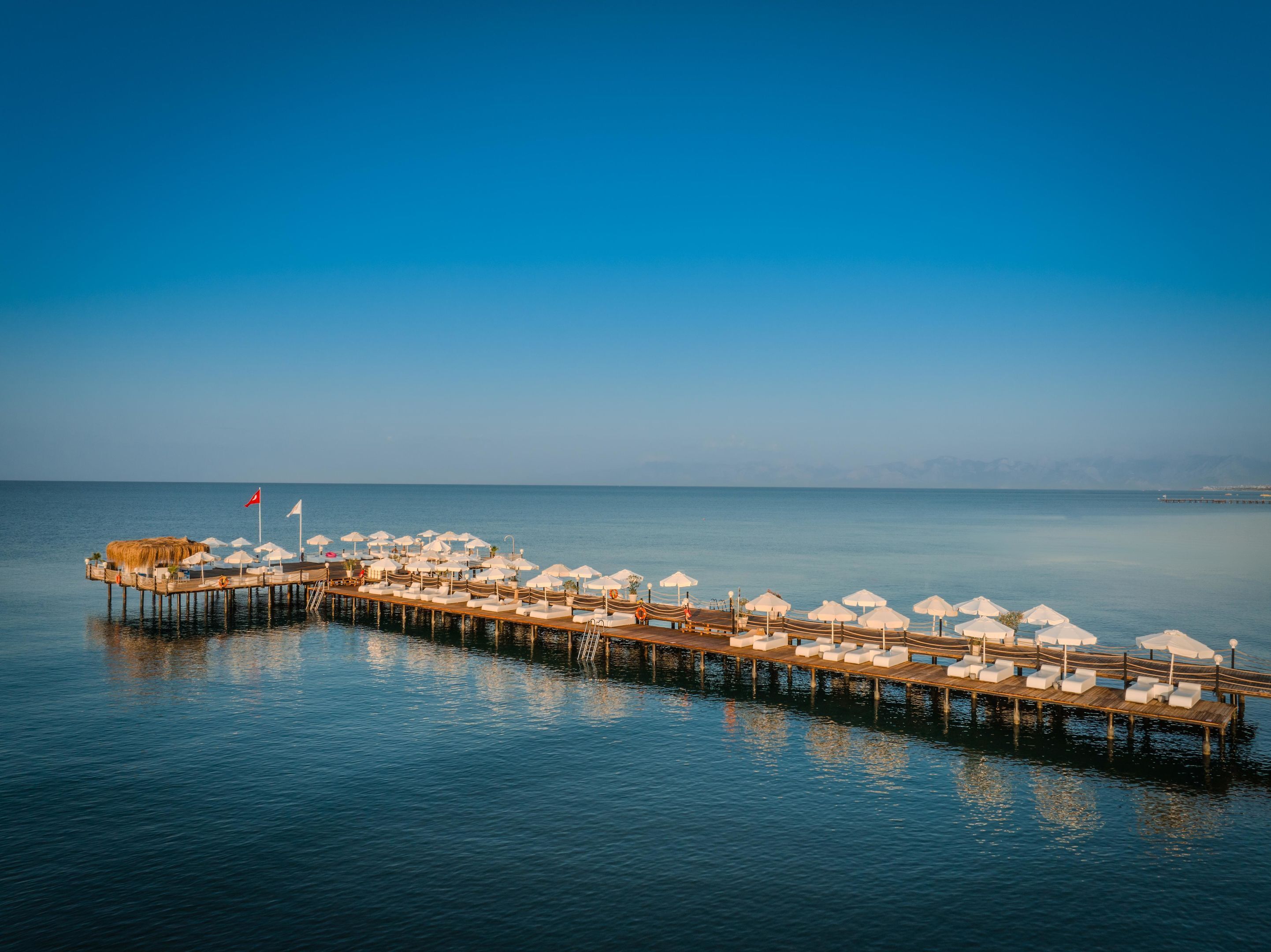 A pier with white umbrellas and lounge chairs extending into calm waters.