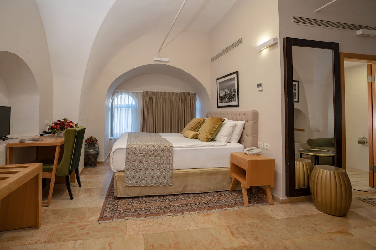 A bedroom with a bed, bedside table, chair, desk, and a large mirror.