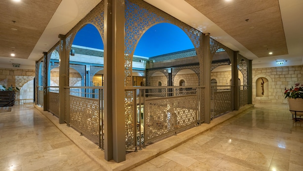 A spacious lobby with a high ceiling, ornate metal railings, and a view of the sky through arched openings.