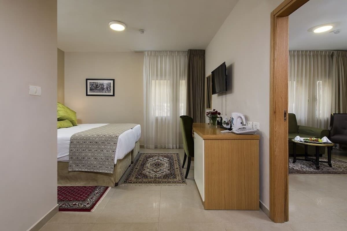 A hotel room with a bed, desk, chair, television, and a view of the outside.