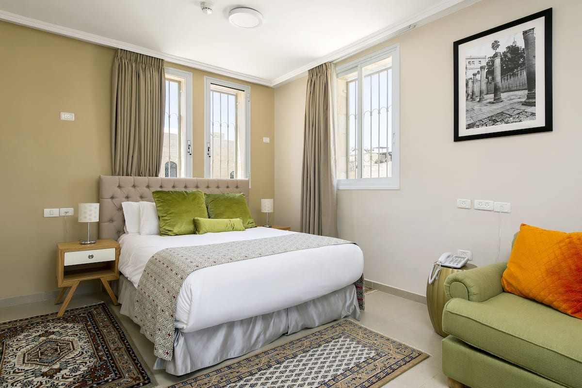 A bedroom with a bed, bedside tables, a green sofa, a patterned rug, and a framed picture on the wall.