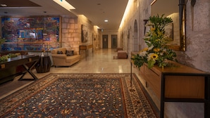 A spacious lobby with a large mosaic artwork, a wooden reception desk, and a patterned rug.