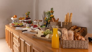 A buffet table with various food items including fruits, cheeses, bread, and a glass of orange juice.