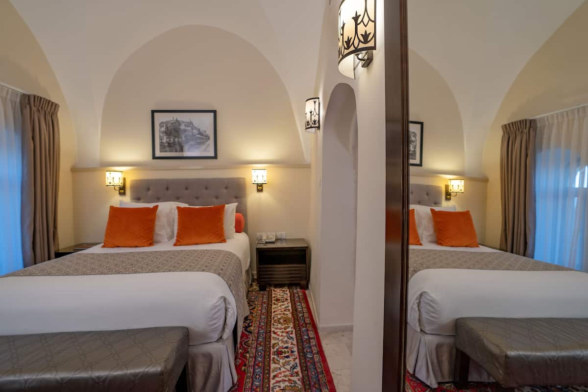 A hotel room with two beds, a large mirror, and a patterned carpet.