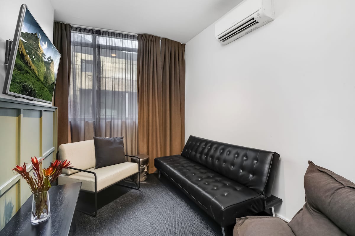 A modern hotel room with a sofa, armchair, and a flat-screen TV on a stand.