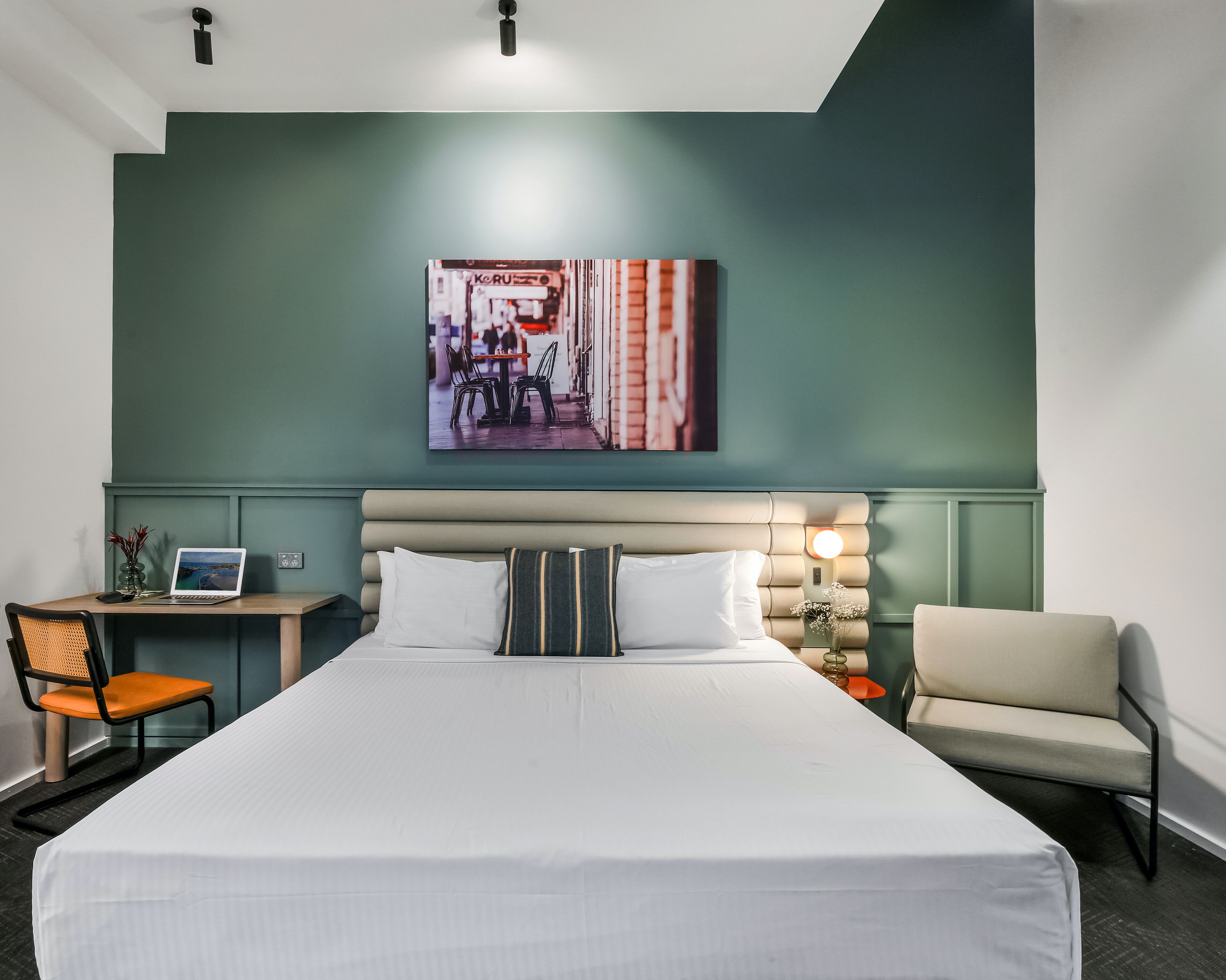 Habitación de hotel con una cama grande, un escritorio con una computadora portátil, una silla, un sofá y una lámpara fijada en la pared.