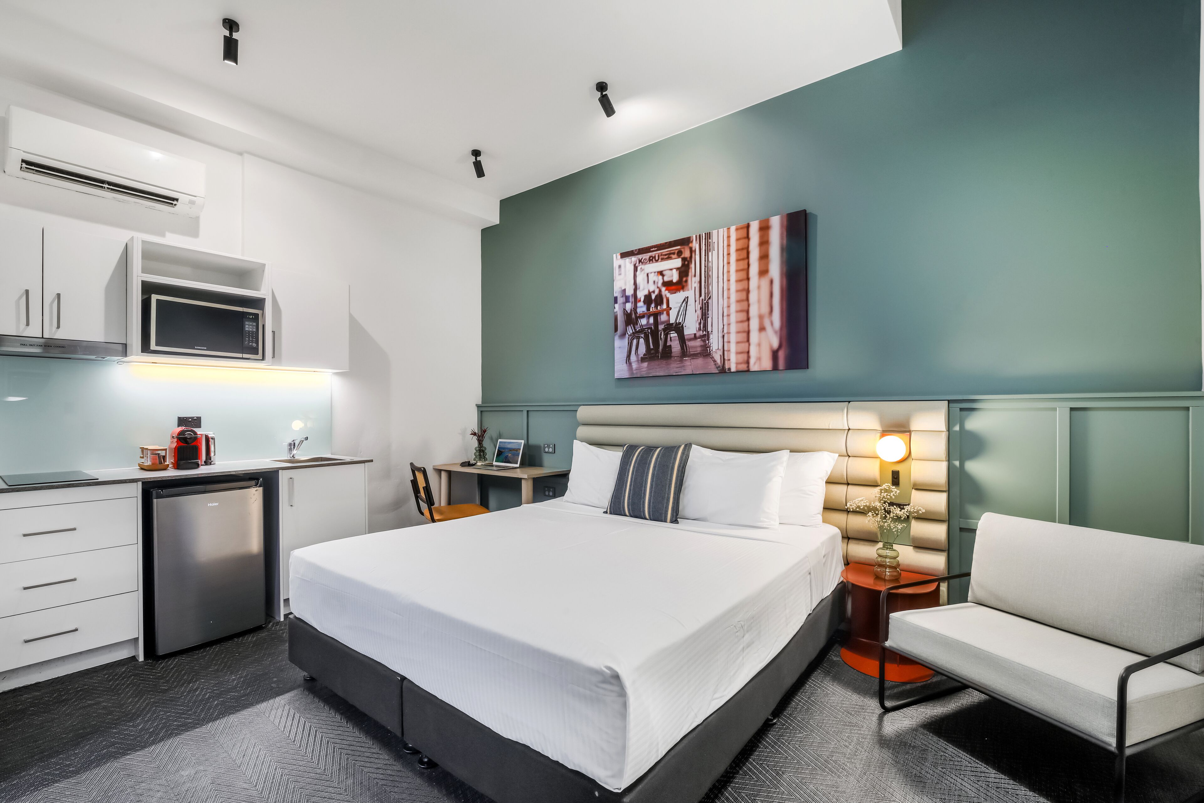 A hotel room with a bed, a desk, a microwave, a refrigerator, and a wall-mounted TV.