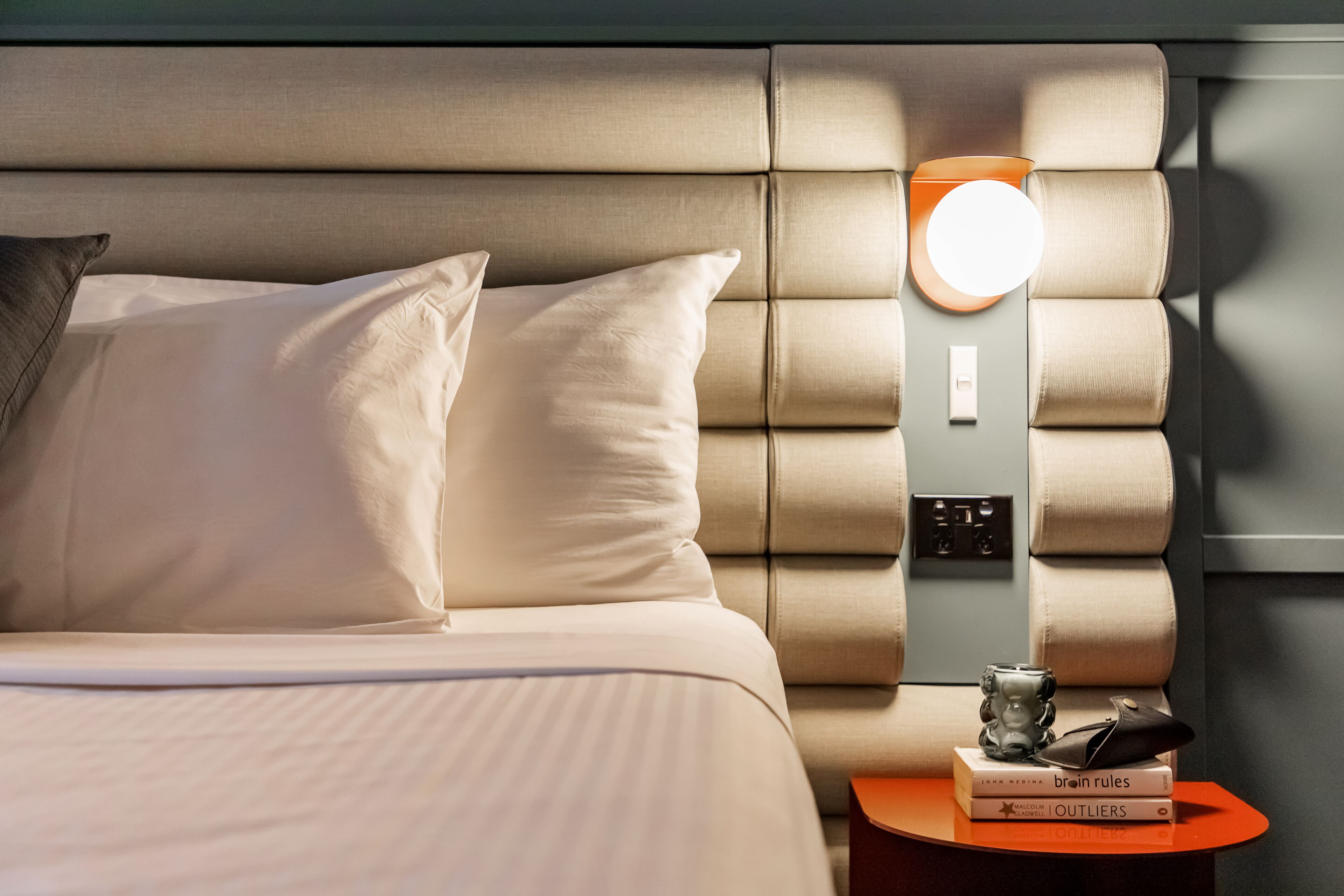 A neatly made bed with pillows, a bedside table with a lamp, and books.