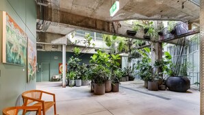 Un vaste espace intérieur doté de piliers en béton, de plantes en pot et de chaises en bois.