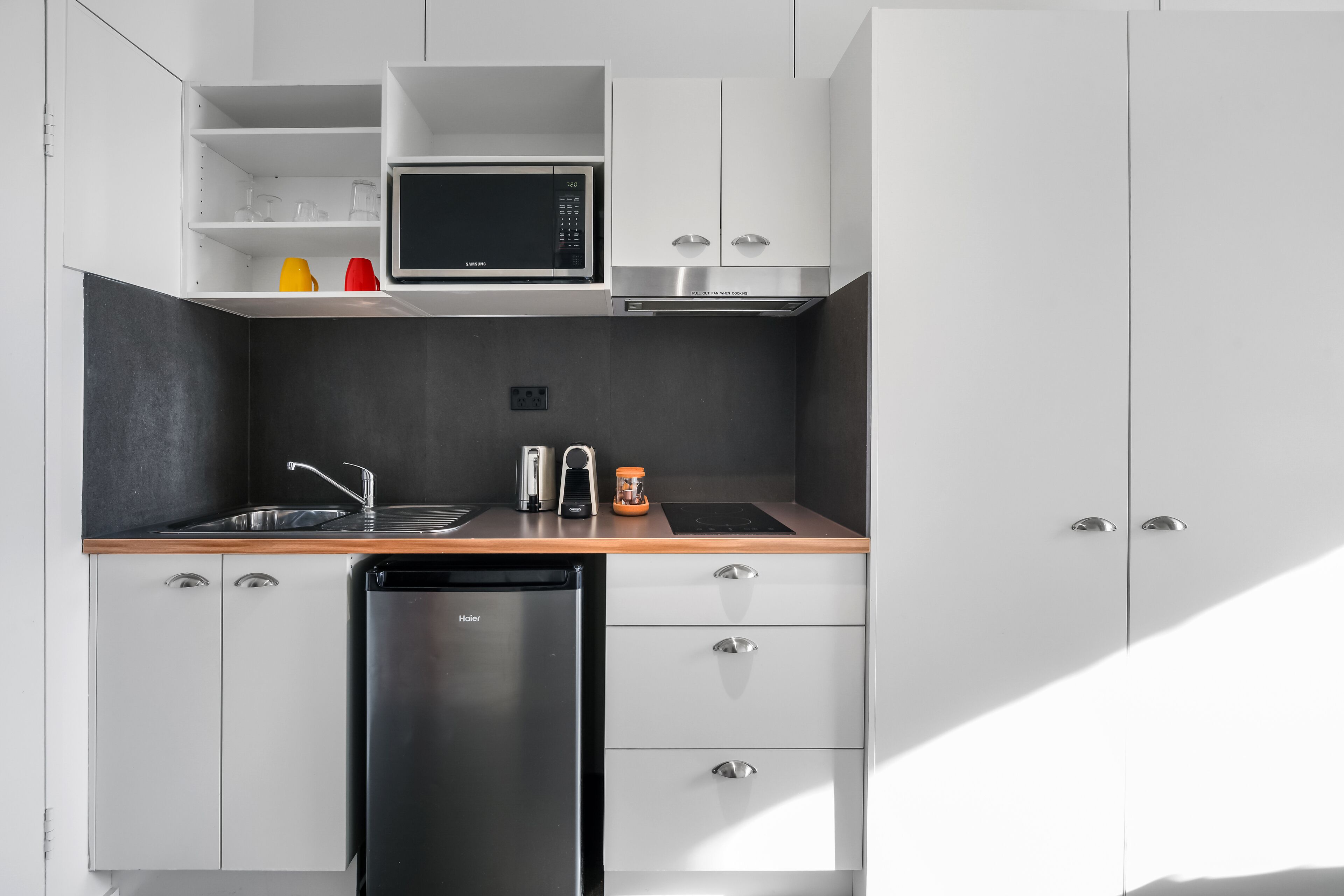 Une cuisine moderne avec des meubles blancs, un lave-vaisselle noir, un four à micro-ondes et une machine à café.