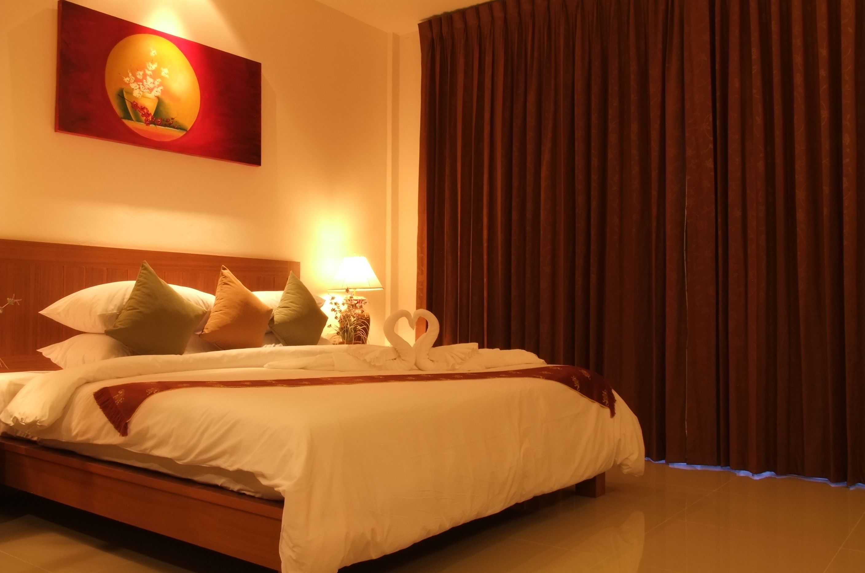 A neatly made bed with white linens, a wooden headboard, and decorative pillows. A wall-mounted lamp and a painting are visible.
