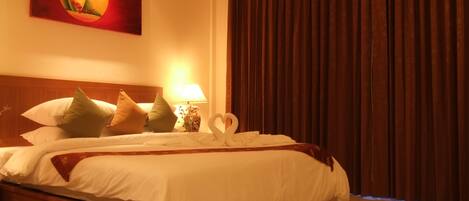 A neatly made bed with white linens, a wooden headboard, and decorative pillows. A wall-mounted lamp and a painting are visible.