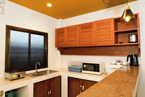 A kitchen with wooden cabinets, a microwave, a kettle, and a sink.