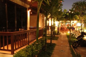 A nighttime outdoor area with a pathway, palm trees, and a seating area with chairs and a motorcycle. - Kata Noi Resort (Karon)