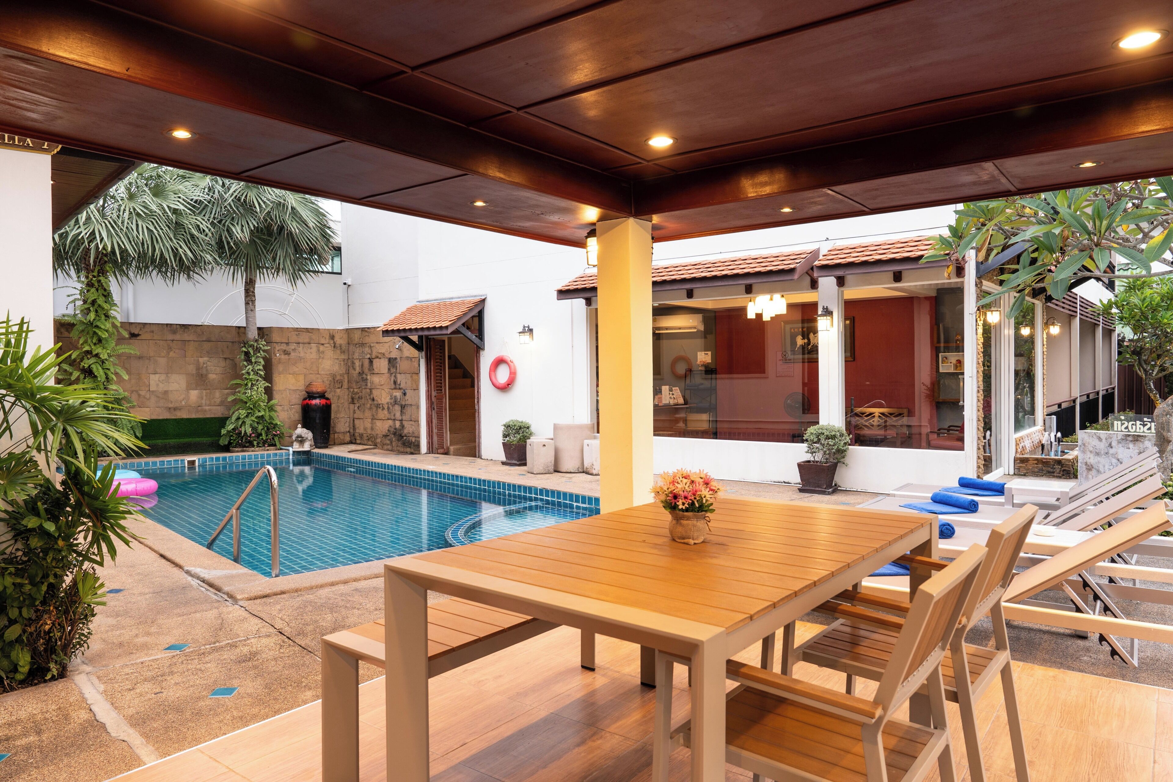 Un espacio al aire libre cubierto con piscina, mobiliario de madera y plantas en macetas.