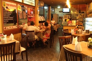 A restaurant with wooden tables and chairs, posters on the walls, and a person standing in the background.