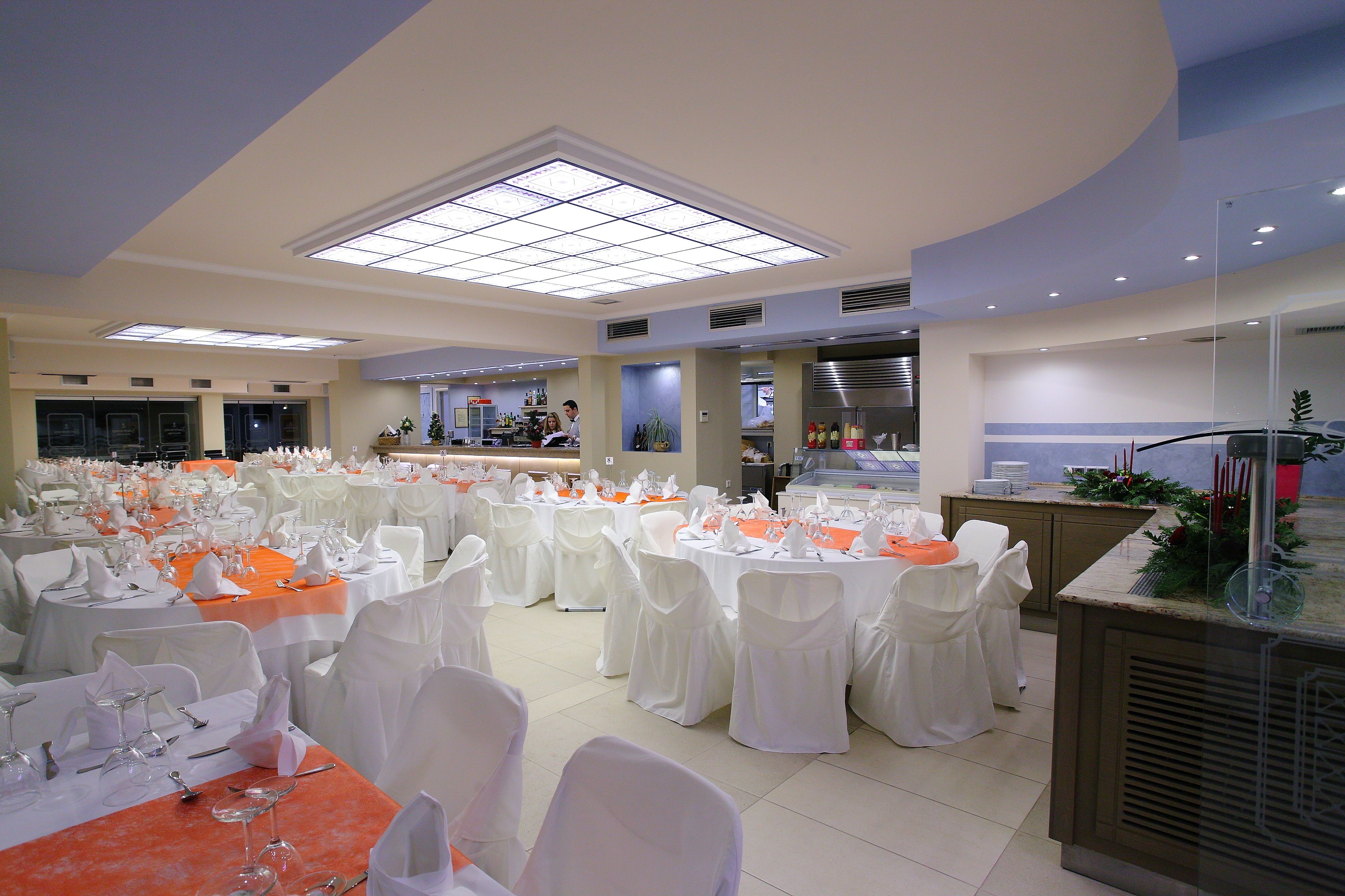 Une salle de banquet avec des tables rondes dressées pour un événement formel, agrémentée de chaises blanches et de nappes orange.