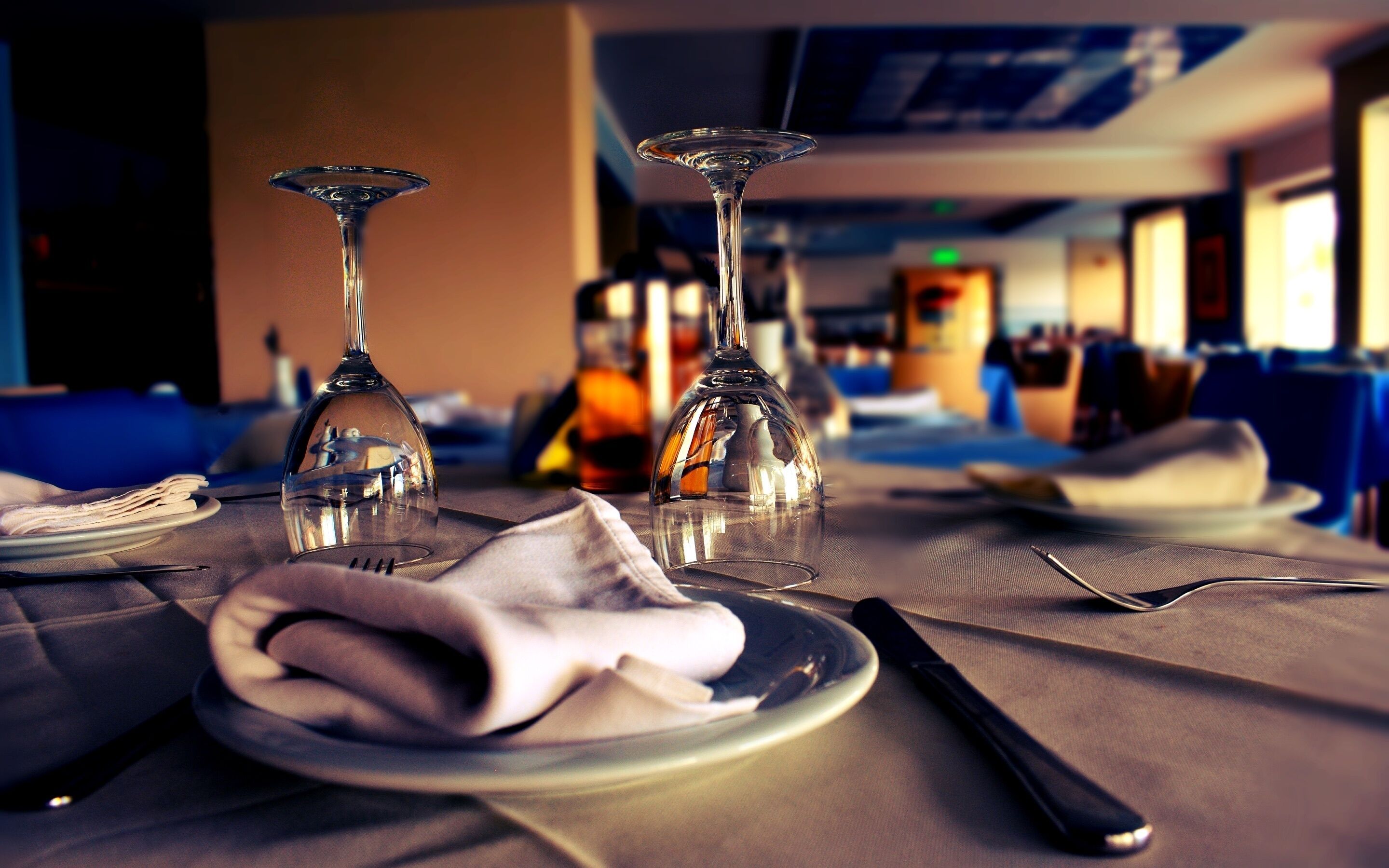 A dining table with two wine glasses, a folded napkin, a plate, and cutlery.