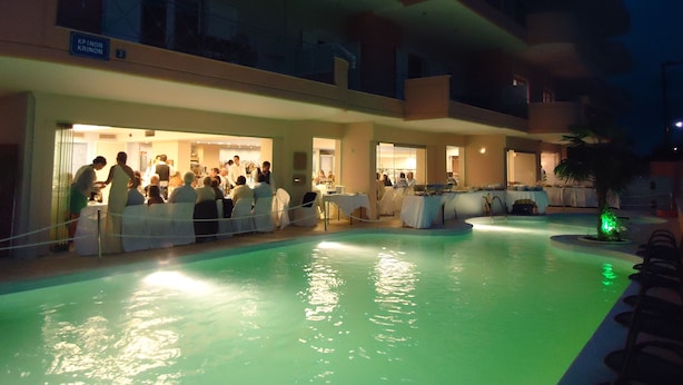 A pool area with a bar and dining area, surrounded by a multi-story building with balconies.