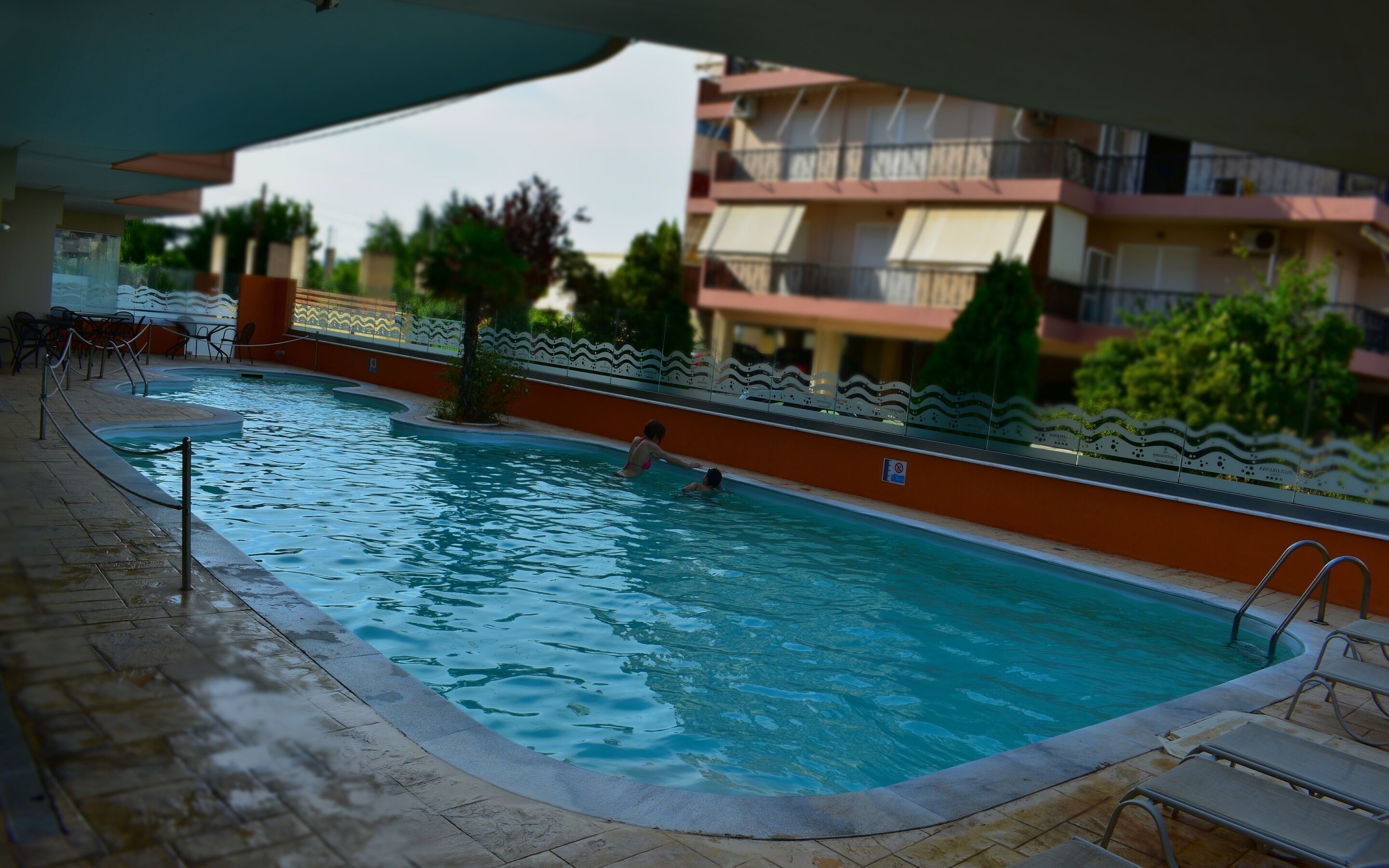 Una piscina con solárium empedrado, una silla de salvavidas y un cartel de prohibido bañarse.