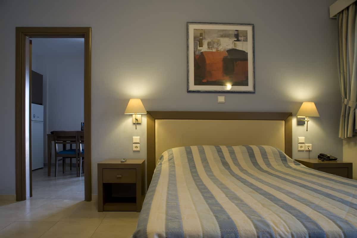 Habitación de hotel con cama, dos lámparas de noche, un cuadro abstracto enmarcado, una mesita y una silla.