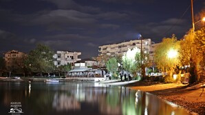 A nighttime view of a waterfront area with buildings, a calm body of water, and street lighting.