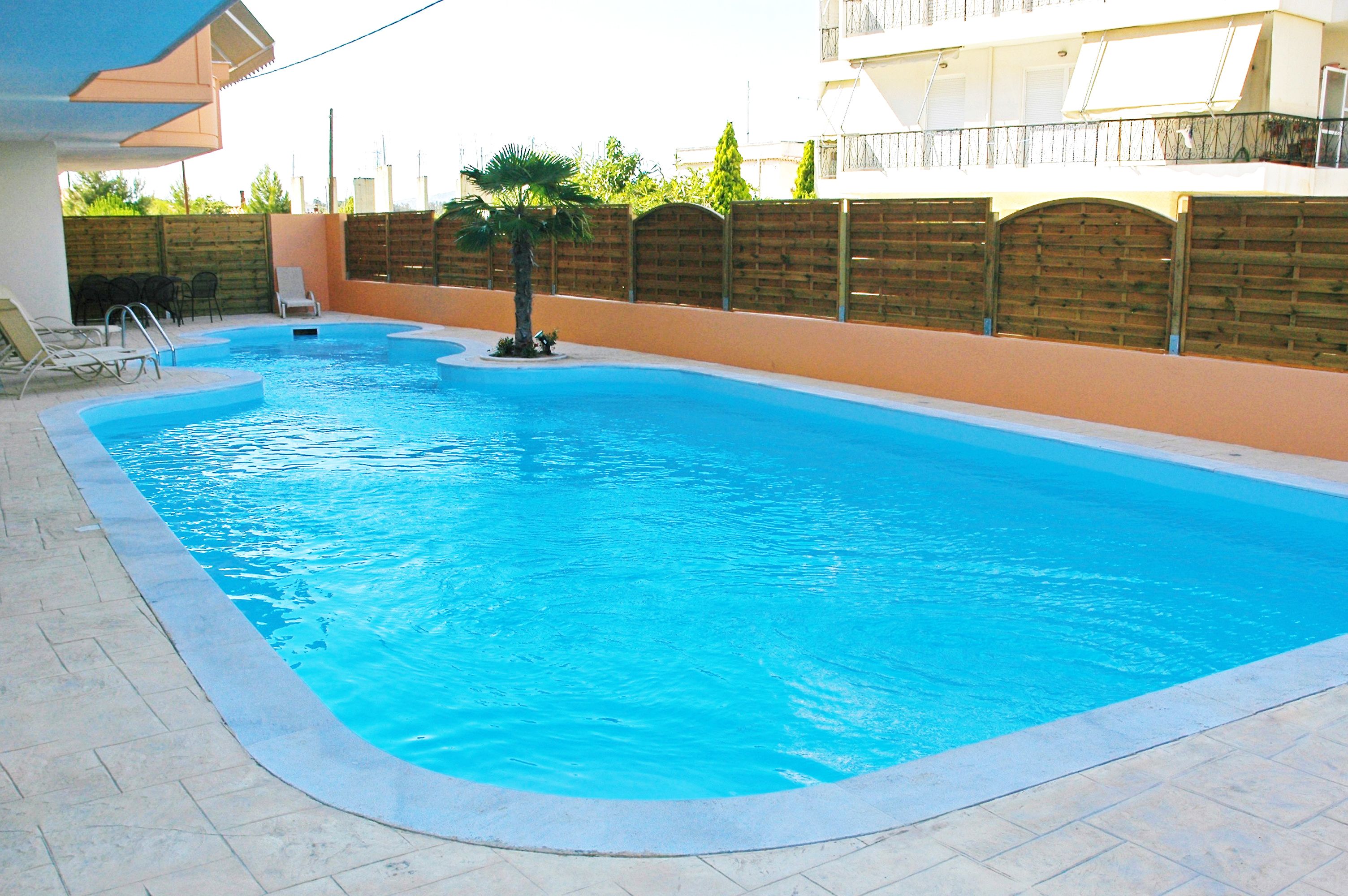 A rectangular swimming pool with a tiled edge, surrounded by a low brick wall and a wooden fence.