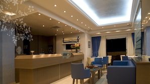 A modern hotel lobby with a reception desk, seating area, and a large skylight.
