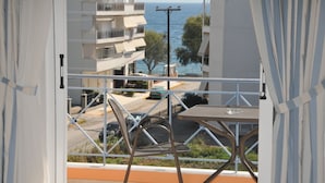 A balcony with a table and chairs, overlooking a street and buildings with a view of the sea.