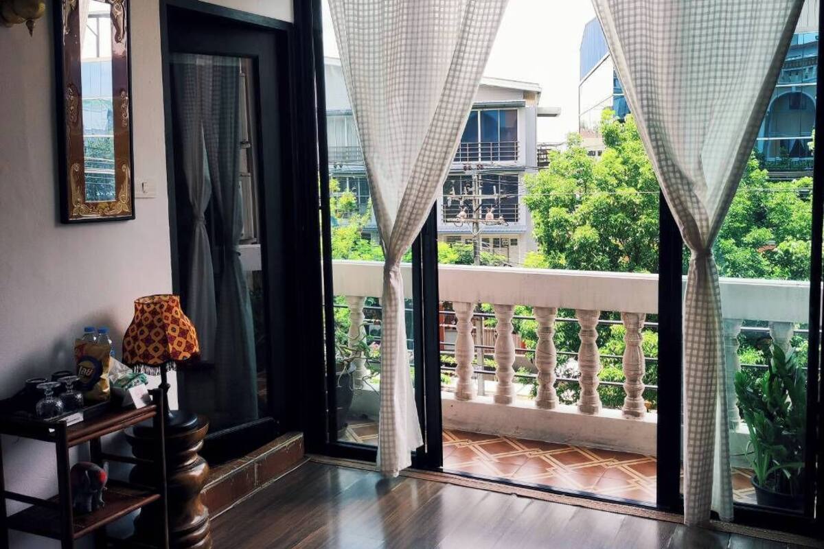A hotel room with a balcony, a bed, a desk with a lamp, and a window with curtains.